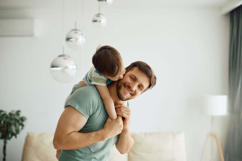 Father carrying his toddler son on his back in a living room - sole physical custody