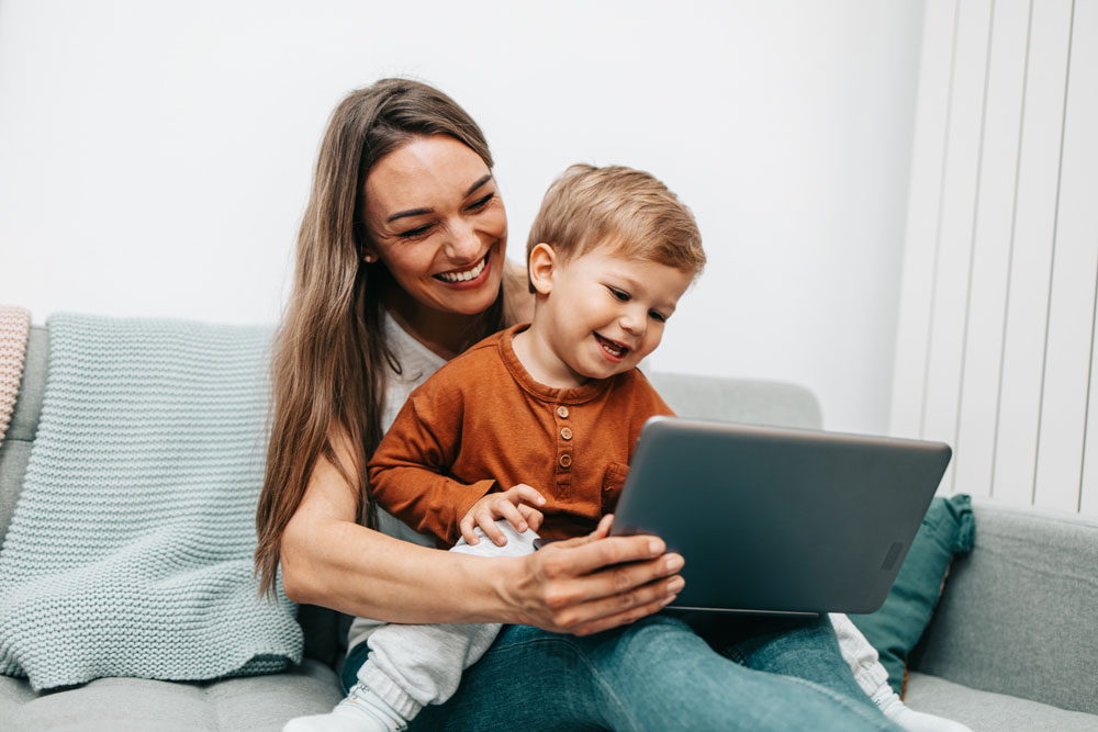 Mother and toddler sitting on a couch happily looking at a computer screen - estate planning and child custody