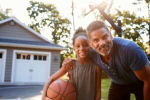 Black father and young daughter playing basketball posing and smiling