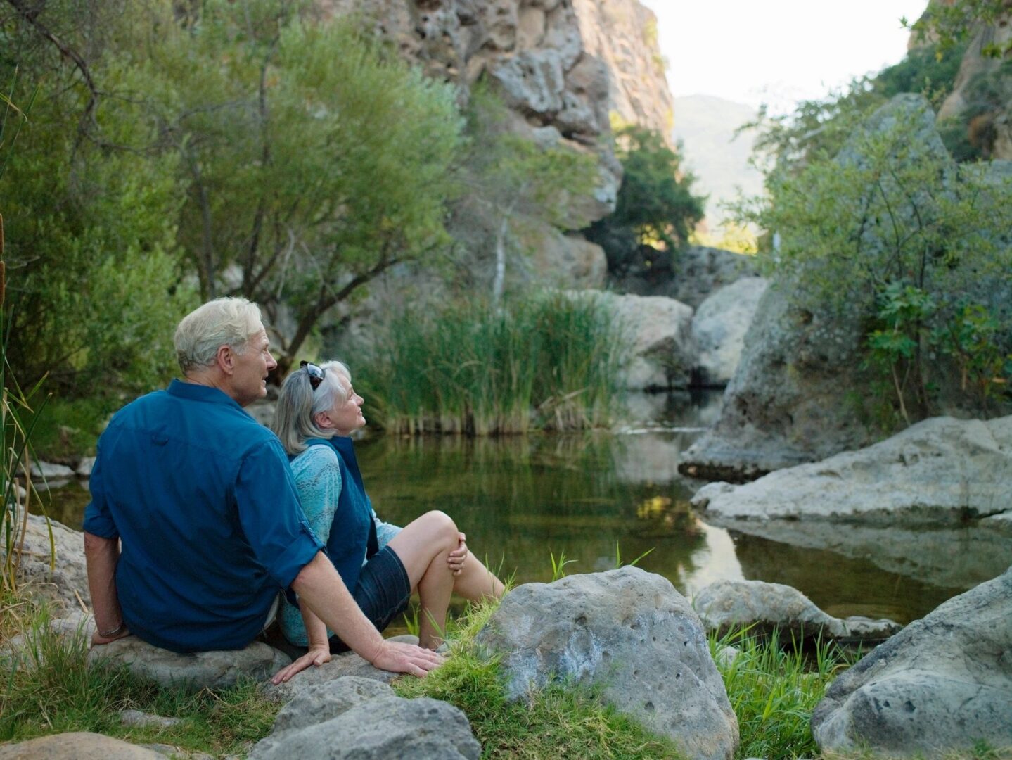 older couple seated on large rocks by a stream